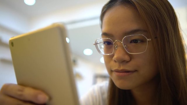 4K Asian Woman is smiling happiness when using tablet touch screen to chat and contact people on the distance in a coffeeshop. Girl checks social network with modern wireless technology in asia-Dan