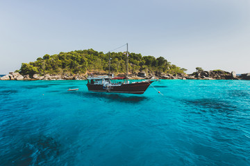 Fototapeta na wymiar Tourist boat near island shore with turquoise clear transparent water. Idyllic view of Similan Islands