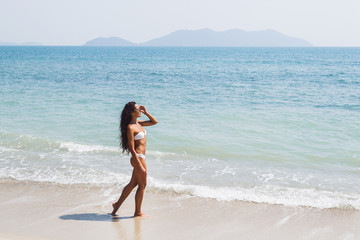 Fototapeta na wymiar Beautiful thin woman with long black hair walking by the amazing white sand beach