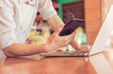 Close up of people hand using smartphone and laptop on wooden table in technology and business concept