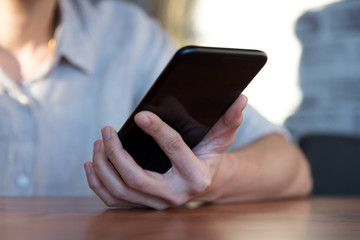 Close up of people hand using smartphone and laptop on wooden table in technology and business concept