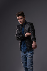 Casual young man in black jacket, jeans and boots on black background. Studio shoot.