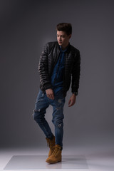 Fototapeta premium Casual young man in black jacket, jeans and boots on black background. Studio shoot.