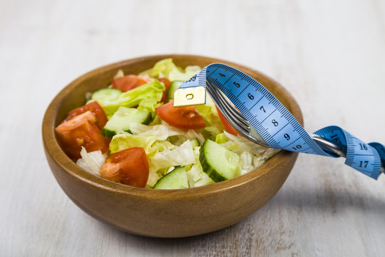 Salad in wooden bowl, fork and measuring tape on a table close-up.