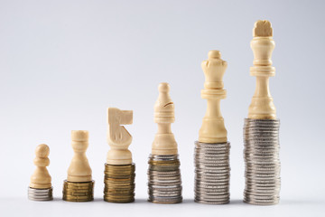 Growing coins stacks on white background. White chess figures standing on coins meaning power and career growth. Financial growth, saving money, business finance wealth and success concept.