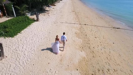 Young Wedding Couple Walking on the Paradise Beach. HD aerial view. Phuket, Thailand.