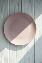 empty pink plate on a wooden table in sunlight rays. texture, background, wallpaper