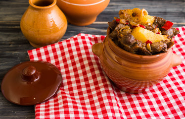 Fried chicken gizzards with potatoes in a clay pot on a wooden background in rustic style