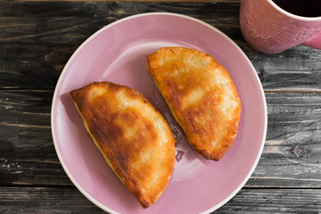 Pasties with meat, and a mug of tea on a wooden table in a rustic style.