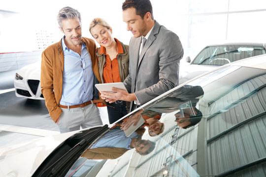 Car seller with couple in car dealership