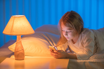 The girl with a phone lay on the bed. Evening night time