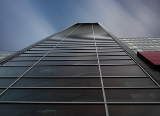 Tall modern glass bussines building with moving clouds and windows reflection.