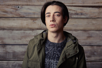 Handsome man wearing green jaket and torn jeans in wooden rural house interior