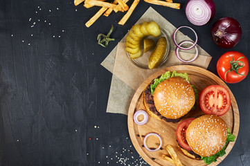 Craft beef burgers on round wooden cutting board with vegetables and french fries. Flat lay on...