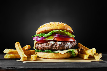 Craft beef burger and french fries on wooden table isolated on black background. - obrazy, fototapety, plakaty