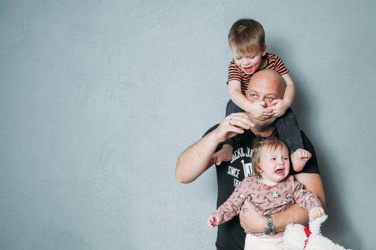 Stressed Young Dad With Two Small Children In His Arms