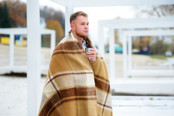 A young man drinking coffee with cup standing on the autumn beach