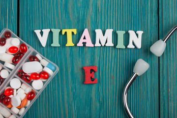 Text "Vitamin E" of colored wooden letters, stethoscope and pills