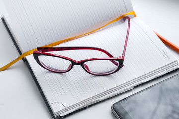 Diary, glasses, orange a pencil and smartphone