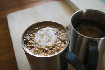 Hot dark coffee in stainless cup with cup of hot tea and stainless spoon on the wood. Dark coffee concept.