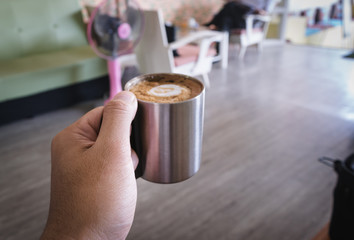 Fototapeta na wymiar Hand holding hot dark coffee in stainless cup in asian coffee shop. Dark coffee concept.
