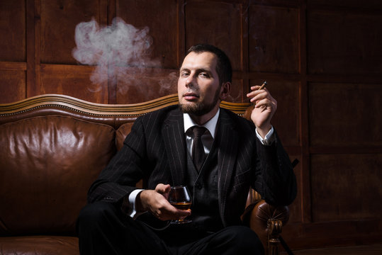 Handsome man is smoking cigar and drinking whiskey