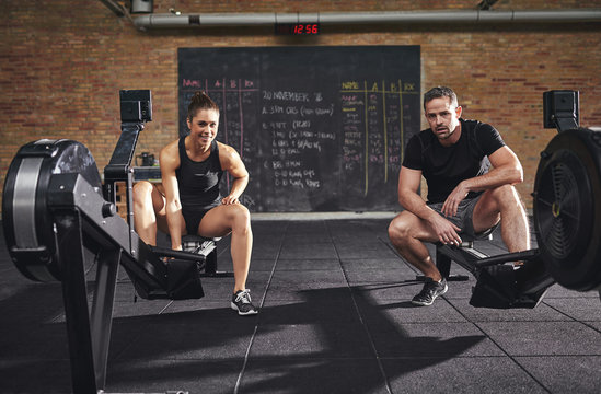 Two confident sportsmen sitting on rowing machines