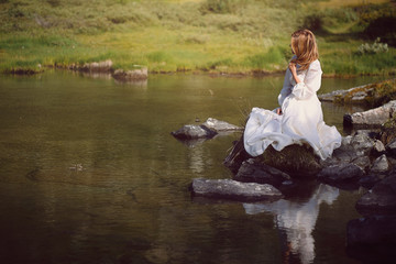 Romantic woman seated on  lake rocks