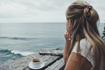 Obraz premium Girl relaxes, drinking coffee and enjoying the view of the ocean, Bali