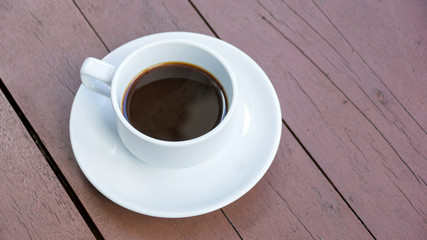 Hot black coffee in a white cup on a wooden table.