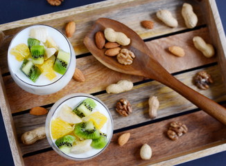 Fresh colorful vitamin breakfast yogurt and assorted mixed nuts, peanuts, almonds, walnuts with pieces of fruits, kiwi, banana, orange, in glass cups