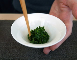 Stir fresh green tea leaves in white cup with chopsticks