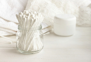 Fototapeta na wymiar Cotton swabs in glass jar, white bathroom towel background. Personal care cleanliness product. 