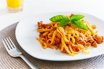 Pasta Bolognese on a plate on a dining table with a glass of fresh orange juice
