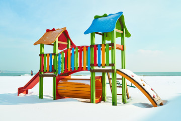 Bright children's playground in the snow on the beach in winter sunny day
