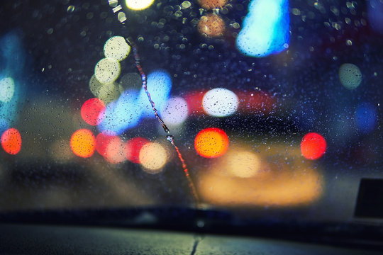Blurred winter picture. Blurred background with the city lights at night. Riding the machine by road. Snowfall in the city. Car windshield wipers clean the snow window