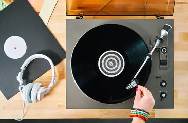 Gramophone with vinyl records and headphones on a wooden table. Hand girl with a bright accessory...