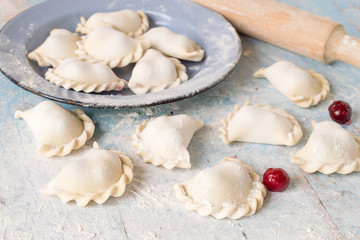Fototapeta na wymiar Homemade dumplings with cherry. Traditional Ukrainian dish. Homemade dumplings with cherry filling in a bowl and on the table, sprinkle with flour.