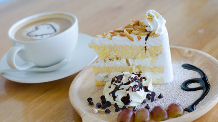 Closeup almond cake and coffee cup with heart shape latte art on wood table