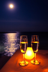 Romantic scene. Two glasses of champagne on the table with candle near the sea under moon light.