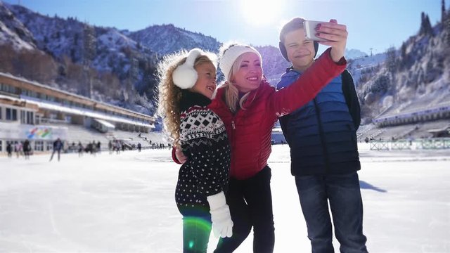 Happy children and mother making selfie by mobile phone, ice skating