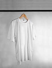 Plain white t-shirt on a wooden clothes hanger. Grey grunge background.
