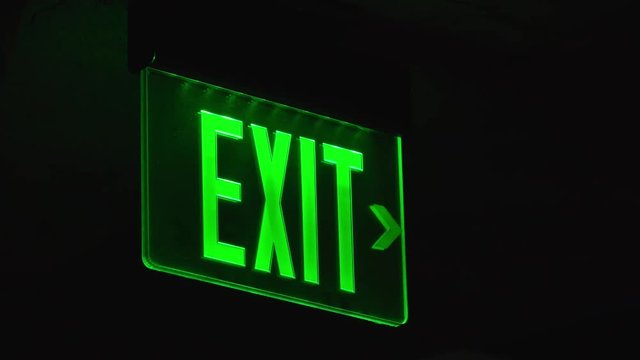Illuminated green exit sign in dark area.
