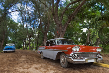 Roter und blauer Oldtimer im Hintergrund in Santa Clara in Kuba - Serie Kuba Reportage