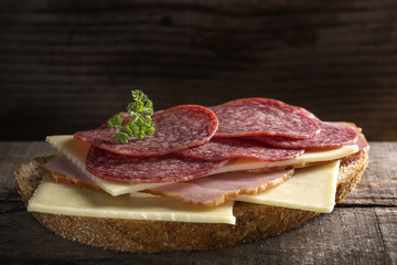 Open sandwich made from cheese, ham and Italian salami on wood