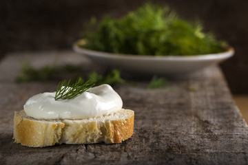Fresh cream cheese on bread slice with dill on wood
