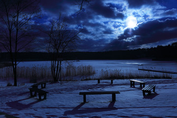 Ławki nad jeziorem zimą, nocą przy księżycu.