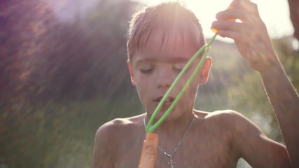 Young boy blowing bubbles outdoors on sunny day in summer on sunshine background with blurred beautiful bokeh. 1920x1080 - Powered by Adobe