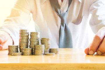 Stack of coins on wooden table over blurred businessman background, business and finance concept