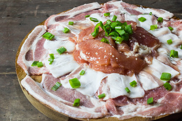 Pieces of raw pork with onion leafs on a wooden plate